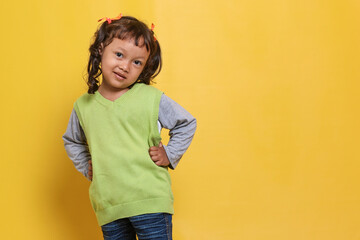 Wall Mural - Portrait of young adorable Asian little girl smiling with hands on waist isolated on yellow background wall with copy space. Education for toddler or preschool, childhood lifestyle 