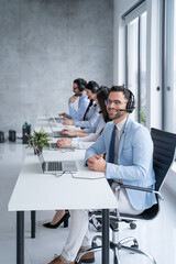 Wall Mural - Call center agent engaging in a conversation with a client, with a headset on, the agent attentively listens to the client's needs while surrounded by supportive colleagues.