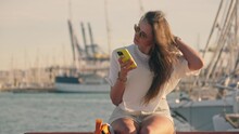A Girl Reads Messages On Her Phone While Sitting On A Bench In A Yacht Club.