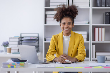 Wall Mural - Young business african american woman office worker analyst sitting at desk working on laptop thinking on project plan, analyzing marketing or financial data online, watching elearning webinar.