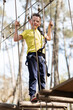 © ADDICTIVE STOCK - Cheerful boy climbing on rope bridge in forest