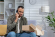© Tetiana - A frustrated African American young man at home talks on the phone with the delivery service, solves problems with the parcel. He looks disappointedly at the open box he is holding in his hands