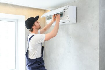 Wall Mural - Smiling young male electrician repair conditioner in client home. Man mechanic or repairman fix filters in air condition device at customer house