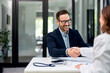 © bnenin - A smiling businessman is shaking hands with a brunette female doctor across the table.