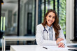 © bnenin - Portrait of a happy female doctor sitting at the office table, dressed in a coat.