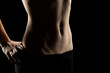 Close-up of a fit woman's stomach under the glow of light in a dark studio background