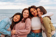 Four young multiracial women in 20s hugging while standing on beach.