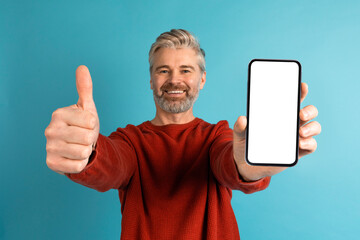 Cheerful middle aged man showing smartphone with mockup, thumb up