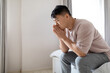 Side view frustrated asian man sitting on bed at home