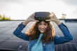 © Halfpoint - Young woman with virtual goggles on the roof with solar panels.
