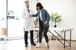 © sofiko14 - Full length view of attractive caucasian man helping young lady in C collar to stand from exam couch leaning on walking cane. Medical specialist supporting patient in consulting room of hospital.