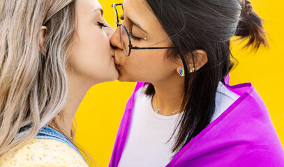 Young lesbian couple in love kissing over yellow background. LGBT festival and gay pride celebration concept.