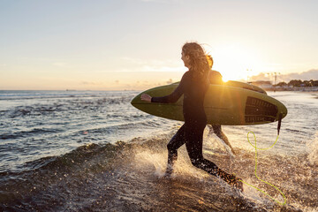 Wall Mural - Surfers running into the ocean to and rushing to catch the waves.