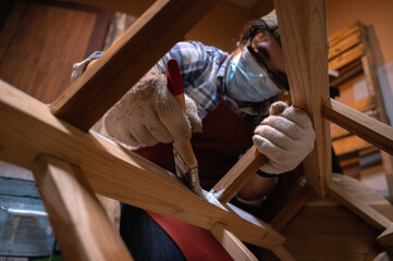 Craftsman, Carpenter using a paintbrush painting to wooden bar chair handmade at woodworking workshop or carpentry workplace. Selective soft focus on the paintbrush.