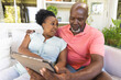 © wavebreak3 - Senior african american couple on couch using tablet and talking in sunny living room