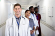 © WavebreakMediaMicro - Unaltered portrait of smiling caucasian male doctor and diverse colleagues in hospital corridor