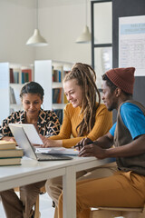 Vertical image of adult students using tablet pc in online studying while sitting at desk in classroom