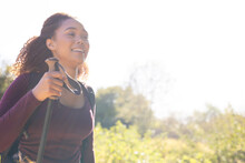 Happy Biracial Woman With Backpack And Trekking Pole, Hiking In Forest, With Copy Space, Unaltered