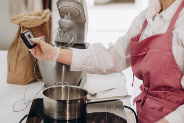 Chef checks the temperature of the heated oil in pot on gas stove with thermometer.