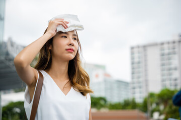 Asian beautiful business woman drying sweat her face with cloth in warm summer day hot weather, Female having sunstroke skin damage from sun UV city air pollution outdoors on street