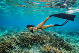 Fototapeta Do akwarium - A young woman in bikini free dives above a coral reef in clear tropical water	