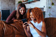 © bernardbodo - Two multiracial best friends using phone and laughing.