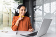 © Liubomir - Young curvy businesswoman with headphones listening to online course and audio podcast female worker inside office working with laptop, successful hispanic woman smiling satisfied with work.
