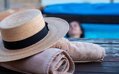 Closeup of a hat and two towels and a girl in the pool in the background