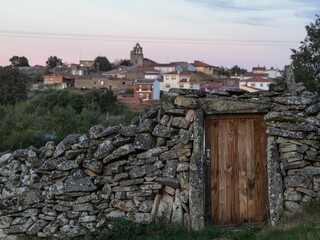 Sticker - Old abandoned stone wall with a wooden door with buildings in the background