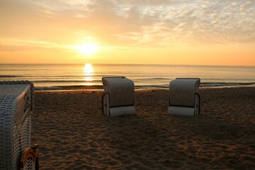 Poster - Straw chairs on the sandy coast of a sea at sunset