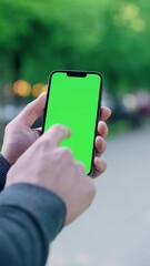 Close Up Man's Hand Holding Phone With Green Mock-up Screen On Background of City Street