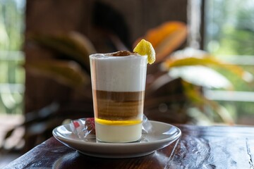 Canvas Print - Horizontal selective focus of a barraquito shot on a brown wooden table with a lemon peel in it