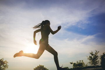 Wall Mural - Silhouette of young woman running sprinting on road with motion blur. Fit runner fitness runner during outdoor workout with sunset background.