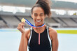 © Emil L/peopleimages.com - Portrait, success medal and women athlete at stadium after winning race or sports event outdoors. Fitness, winner and female runner happy with victory, goals or target achievement on track field.