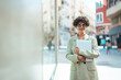 © Dragana Gordic - Curly haired business lady is embracing and holding a laptop while posing with glasses in front of a building. Attractive business woman with laptop walking on city street.