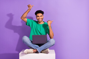 Wall Mural - Full body photo of young man wear green t-shirt direct fingers empty space with laptop sit box netbook apps isolated on purple background