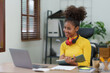 © amnaj - Beautiful young black woman using laptop computer at home. Young woman curly hair working on laptop and take note at home.