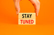 Stay tuned symbol. Concept words Stay tuned on wooden blocks on beautiful orange table orange background. Businessman hand. Business, support, motivation, psychological stay tuned concept. Copy space.