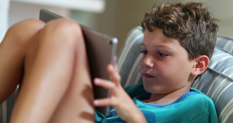 Wall Mural - Child using tablet on couch. Candid young boy playing and browsing internet on new media