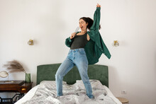 Young Caucasian happy woman is singing and dancing on bed. Funny enjoy in bedroom. Concept of dance and vocals learning