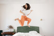 Happy young Caucasian woman funny jumping on bed and play on air guitar. Concept of happiness and fun
