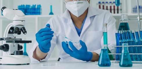 medical or scientific researcher researching and experimenting Multi-colored solution, vial and microscope In the laboratory or in the laboratory by wearing blue gloves and white clothing completely.