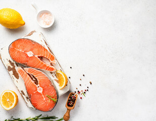 Wall Mural - Fresh raw salmon steaks with spices and lemons on wooden board. Top view of fish on white background.