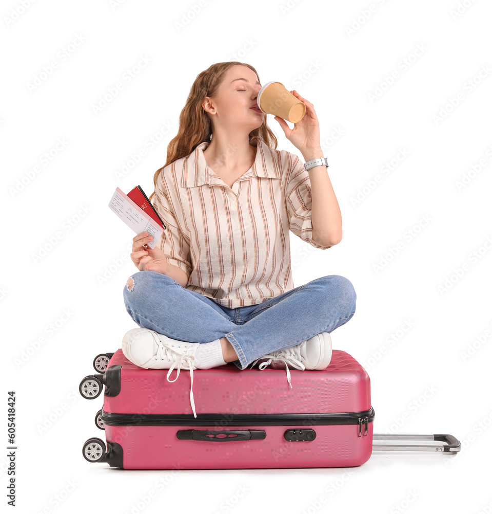 Young woman with passport and suitcase drinking coffee on white background