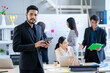 © narong - Portrait of Asian business man with beard stand with hold the tablet and look at camera also stay in front of other co-worker work in the back in office.