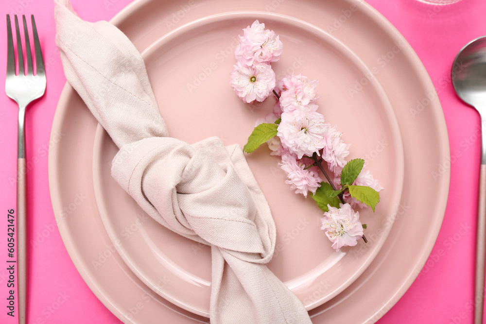 Beautiful table serving with cutlery, blooming tree branch and folded napkin on pink background