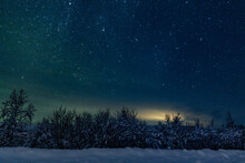 Landscape Of The Night Sky With Bright Stars And Green Northern Lights On The Background Of The Road, Trees, Nature, Snow In Winter