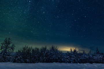 landscape of the night sky with bright stars and green northern lights on the background of the road