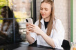© zvkate - Blonde happy woman smiling reading good news on mobile phone during rest in coffee shop, happy caucasian female watching her photos on cell telephone while relaxing in cafe during free time, banking.