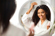 Smiling Black Woman Applying Serum For Hair Repair While Standing Near Mirror
